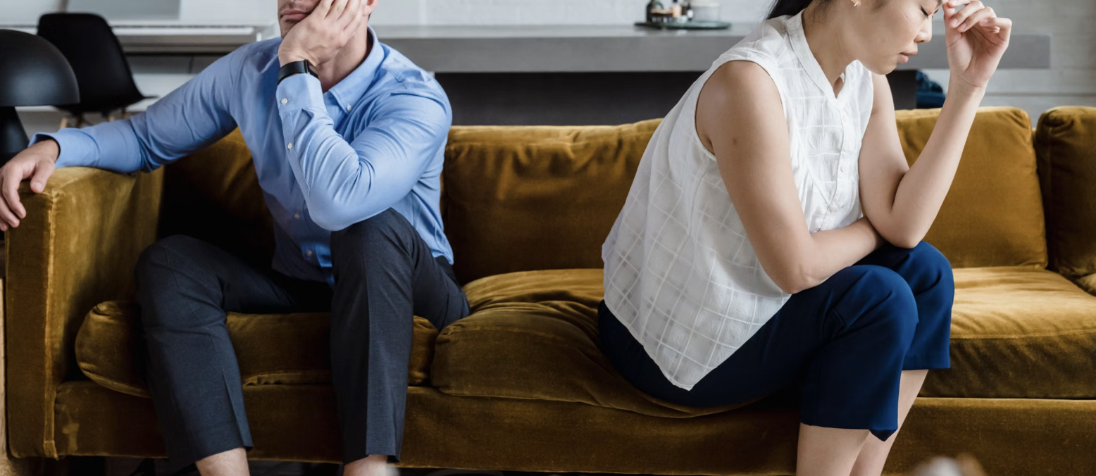 A couple sitting at opposite ends of a sofa, turned away from one another